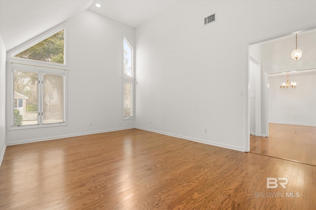 spare room featuring high vaulted ceiling, a chandelier, and hardwood / wood-style floors