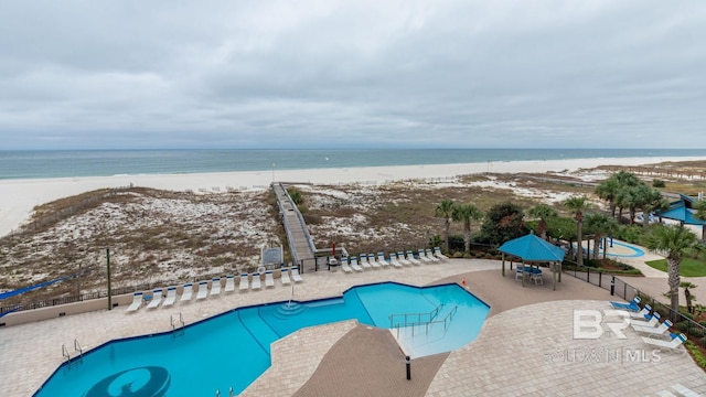 view of swimming pool featuring a beach view, a water view, and a patio area