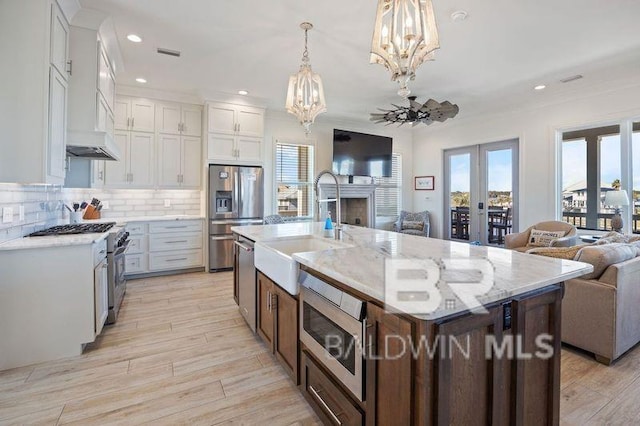 kitchen featuring appliances with stainless steel finishes, decorative light fixtures, white cabinetry, and a kitchen island with sink