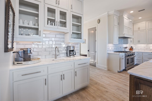 kitchen featuring range with two ovens, sink, light stone countertops, tasteful backsplash, and white cabinetry