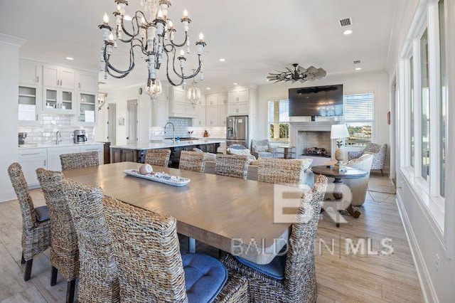 dining room featuring ceiling fan with notable chandelier, light hardwood / wood-style floors, ornamental molding, and sink