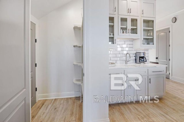 interior space featuring light stone countertops, tasteful backsplash, sink, light hardwood / wood-style flooring, and white cabinetry