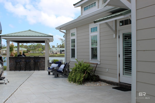 view of patio / terrace with a gazebo, a bar, area for grilling, and a water view