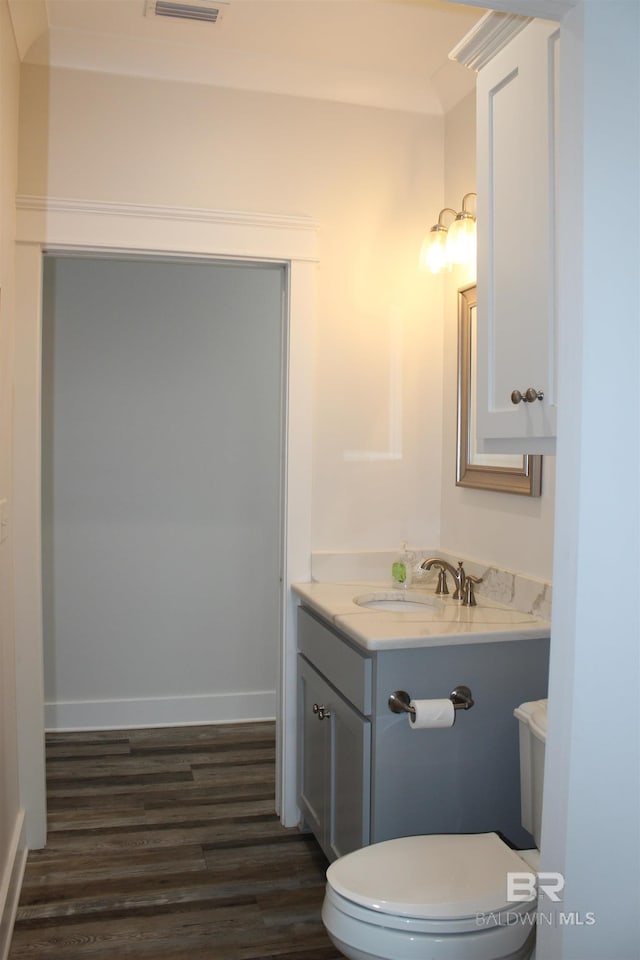 half bathroom with toilet, visible vents, baseboards, wood finished floors, and vanity