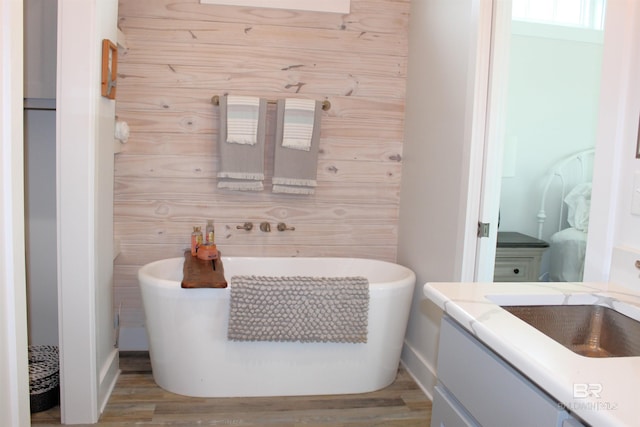 full bathroom with baseboards, wood finished floors, a soaking tub, and vanity
