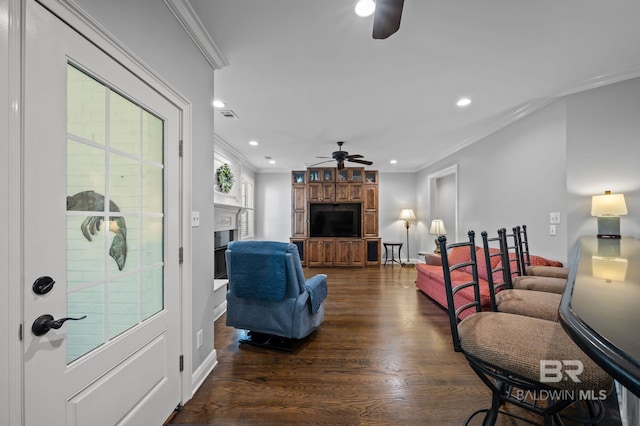 living area with crown molding, ceiling fan, dark wood-style flooring, and a fireplace