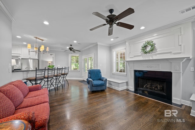 living area with visible vents, ornamental molding, ceiling fan, dark wood finished floors, and a fireplace with flush hearth