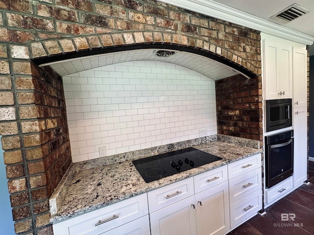 kitchen with white cabinets, black appliances, brick wall, light stone counters, and lofted ceiling