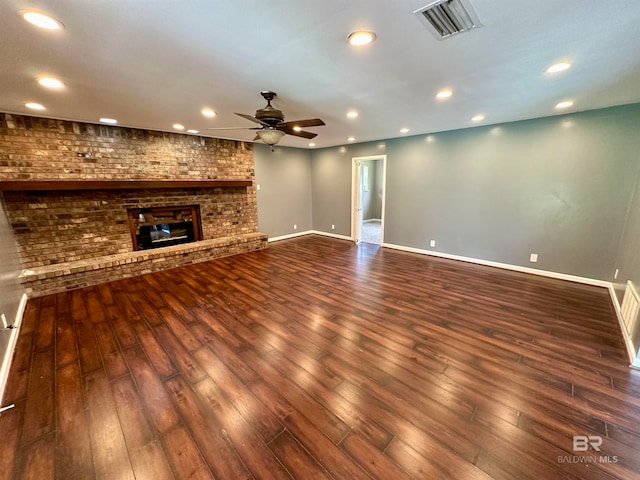 unfurnished living room featuring dark hardwood / wood-style floors, ceiling fan, brick wall, and a brick fireplace