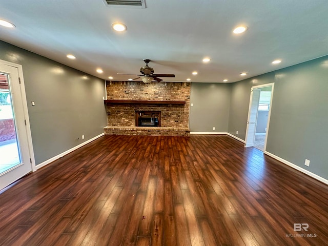 unfurnished living room featuring hardwood / wood-style flooring, brick wall, a brick fireplace, and ceiling fan