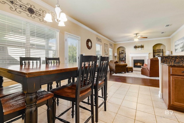 dining area with a tile fireplace, crown molding, light wood-type flooring, and ceiling fan with notable chandelier