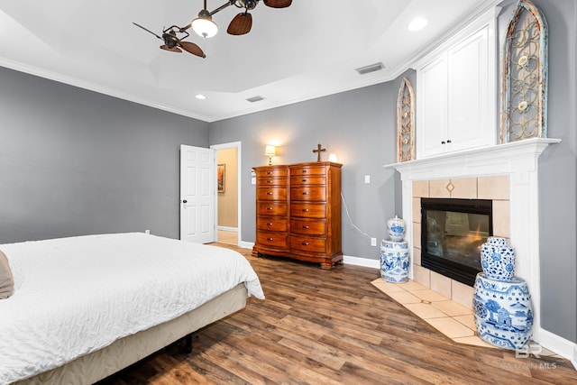 bedroom with dark wood-type flooring, ceiling fan, ornamental molding, and a fireplace