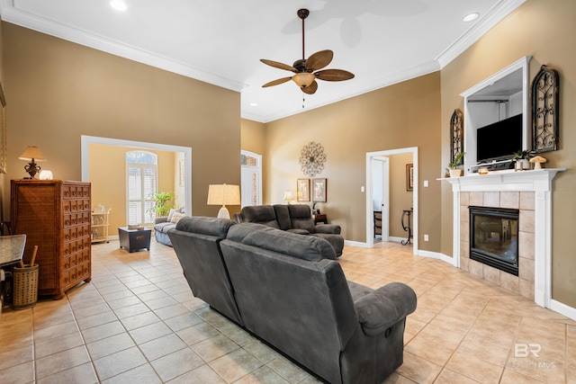 tiled living room featuring a tiled fireplace, crown molding, a towering ceiling, and ceiling fan