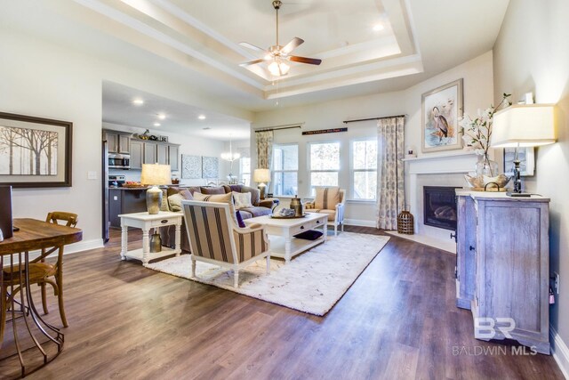 11547 Thistledown Loop, Spanish Fort, AL 36527 - living area with a raised ceiling, a ceiling fan, a fireplace with flush hearth, dark wood-type flooring, and baseboards
