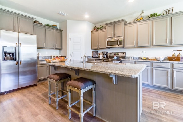11547 Thistledown Loop, Spanish Fort, AL 36527 - kitchen featuring appliances with stainless steel finishes, a sink, a breakfast bar, light wood-style flooring, and light stone countertops