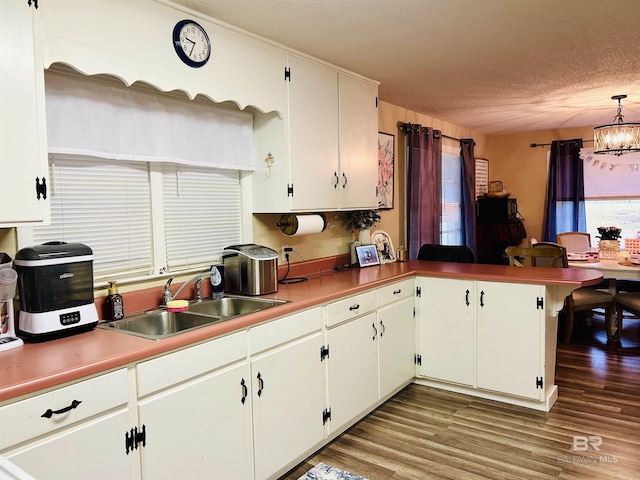 kitchen featuring sink, white cabinetry, kitchen peninsula, hanging light fixtures, and a chandelier