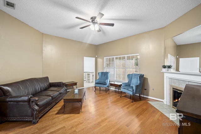 living area featuring wood finished floors, a ceiling fan, visible vents, a tile fireplace, and a textured ceiling