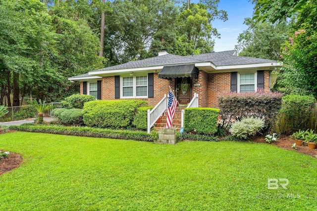 view of front of house with brick siding, a front lawn, a chimney, and a shingled roof