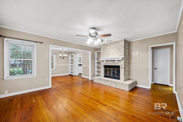 unfurnished living room featuring ceiling fan, ornamental molding, wood finished floors, a brick fireplace, and built in shelves