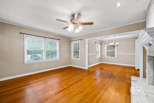 unfurnished living room featuring hardwood / wood-style flooring, ceiling fan with notable chandelier, crown molding, and a fireplace