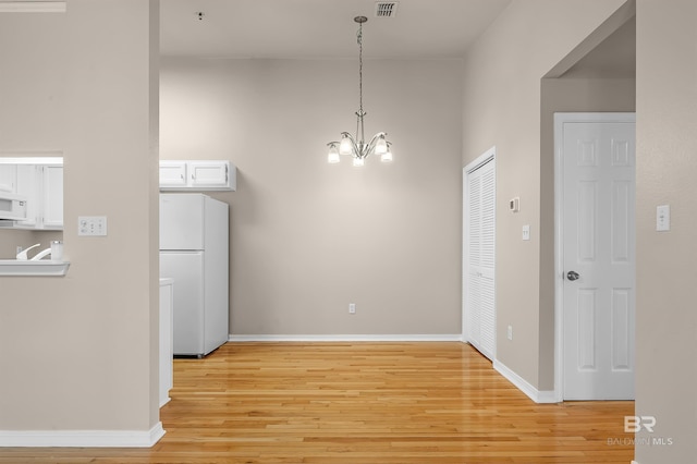 unfurnished dining area with a chandelier, light wood-type flooring, and baseboards