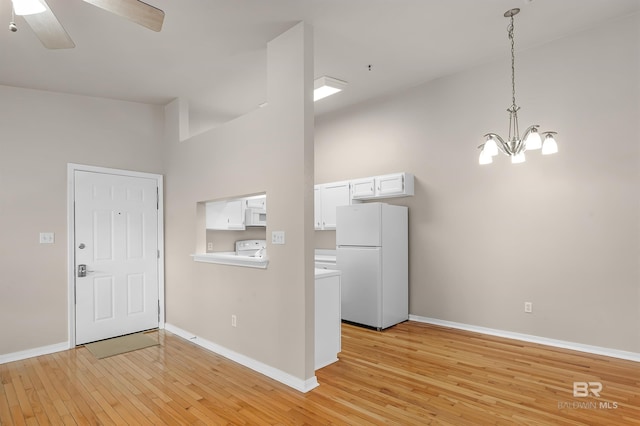 foyer entrance featuring ceiling fan with notable chandelier, a towering ceiling, light wood-style flooring, and baseboards