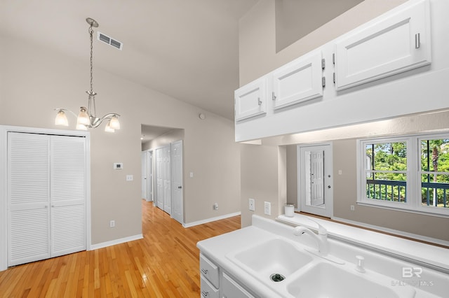 kitchen featuring visible vents, white cabinets, hanging light fixtures, light countertops, and a sink