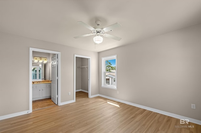 unfurnished bedroom featuring a sink, baseboards, a spacious closet, a closet, and light wood-type flooring