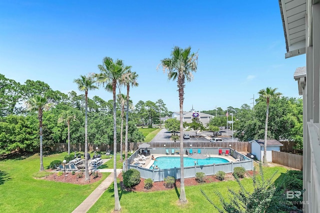 pool with a fenced backyard, an outdoor structure, a lawn, and a storage unit