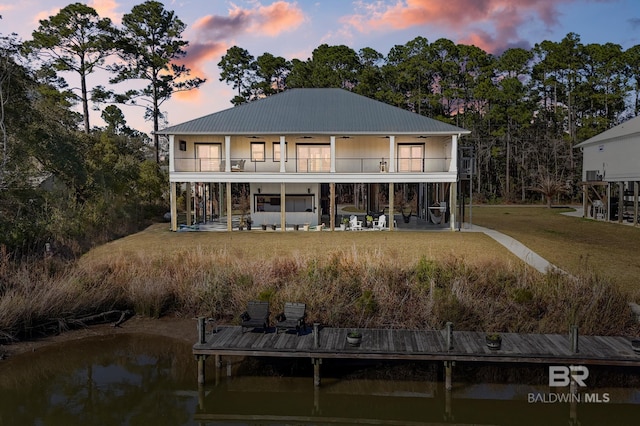 back house at dusk featuring ceiling fan, a lawn, a patio area, and a balcony