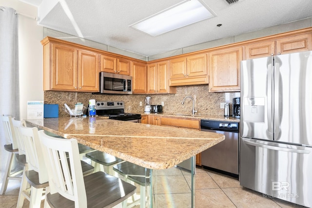 kitchen with light tile patterned floors, a kitchen bar, kitchen peninsula, appliances with stainless steel finishes, and sink