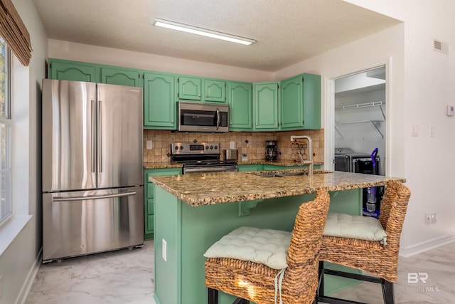 kitchen featuring a kitchen breakfast bar, sink, green cabinetry, washing machine and dryer, and appliances with stainless steel finishes