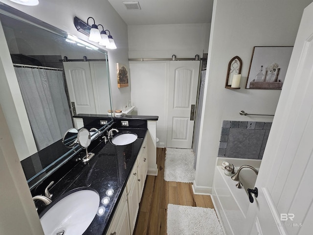 bathroom featuring a garden tub, a sink, visible vents, and wood finished floors