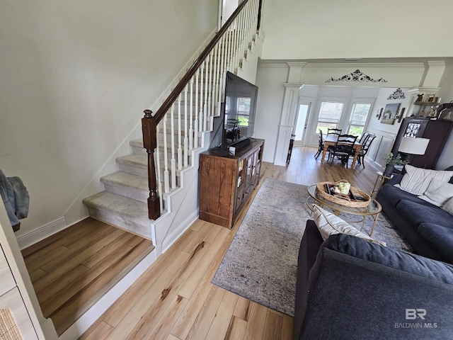 living area with a towering ceiling, baseboards, stairway, light wood finished floors, and ornate columns