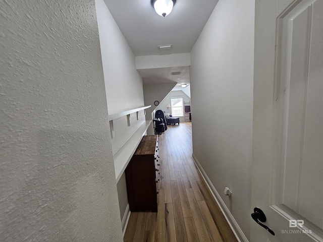 hallway with visible vents, a textured wall, baseboards, and wood finished floors