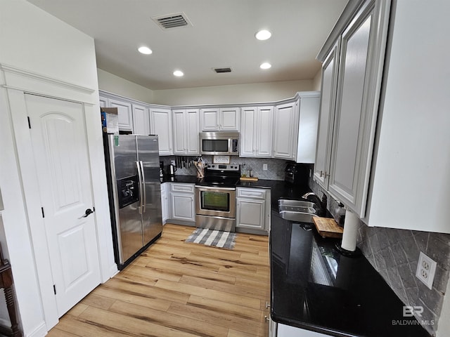 kitchen with stainless steel appliances, a sink, visible vents, light wood-style floors, and dark countertops