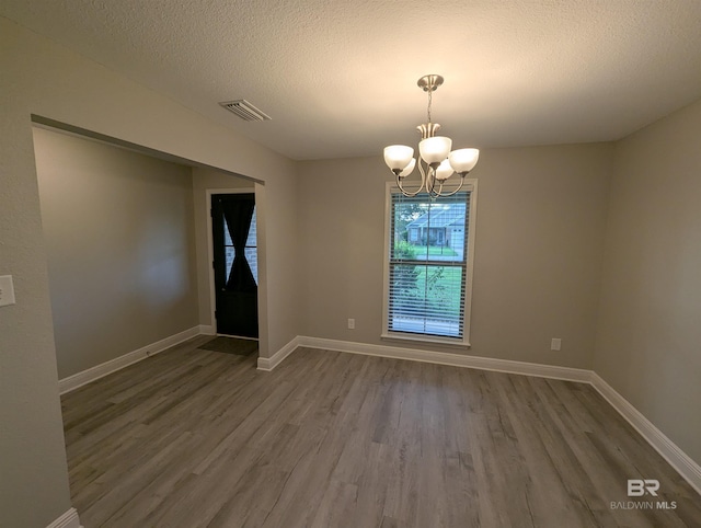 empty room with a textured ceiling, baseboards, a notable chandelier, and wood finished floors