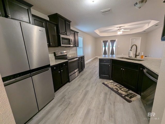 kitchen featuring visible vents, a raised ceiling, appliances with stainless steel finishes, dark cabinets, and a sink