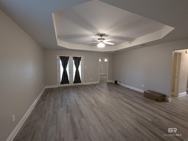 unfurnished room with wood finished floors, visible vents, a ceiling fan, baseboards, and a tray ceiling