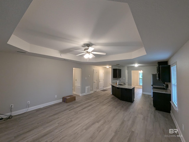 unfurnished living room with a tray ceiling, ceiling fan, baseboards, and wood finished floors