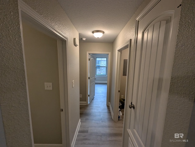 corridor featuring baseboards, wood finished floors, a textured ceiling, and a textured wall