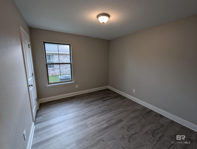 empty room featuring dark wood finished floors, a textured ceiling, and baseboards