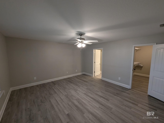 unfurnished bedroom featuring visible vents, baseboards, a walk in closet, and wood finished floors