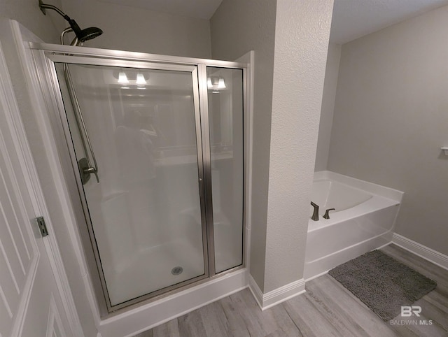 full bath featuring baseboards, a shower stall, a bath, and wood finished floors