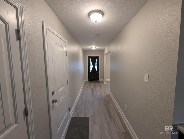 hall featuring a textured wall, a textured ceiling, baseboards, and wood finished floors