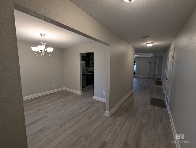 corridor with visible vents, a textured ceiling, baseboards, and wood finished floors