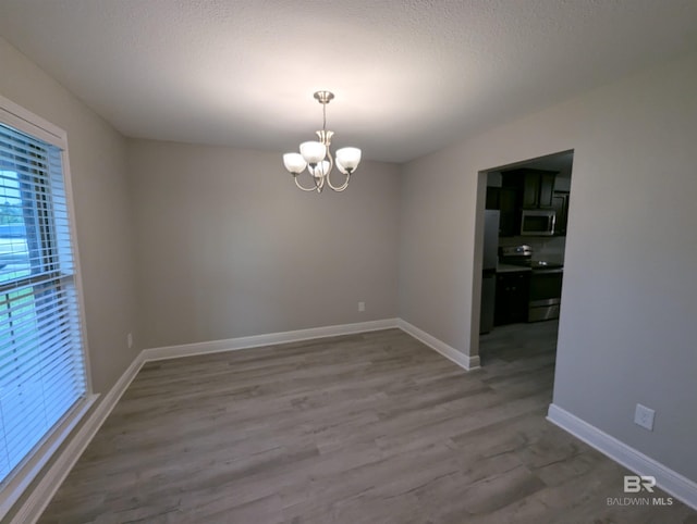 empty room featuring an inviting chandelier, a textured ceiling, baseboards, and wood finished floors