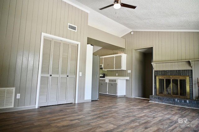 unfurnished living room with lofted ceiling, dark hardwood / wood-style flooring, ceiling fan, a brick fireplace, and a textured ceiling