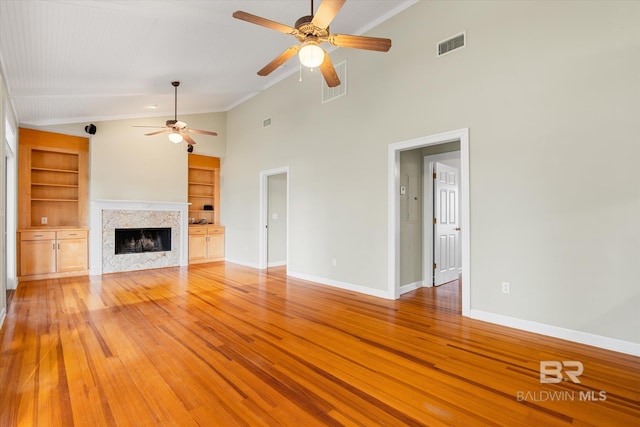 unfurnished living room with built in shelves, ceiling fan, high vaulted ceiling, and light hardwood / wood-style floors