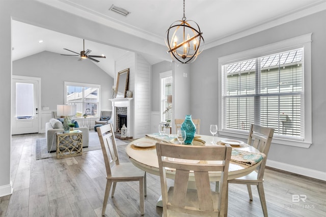23901 Cypress Xing, Orange Beach, AL 36561 - dining space with a fireplace, light wood-style flooring, vaulted ceiling, and ceiling fan with notable chandelier